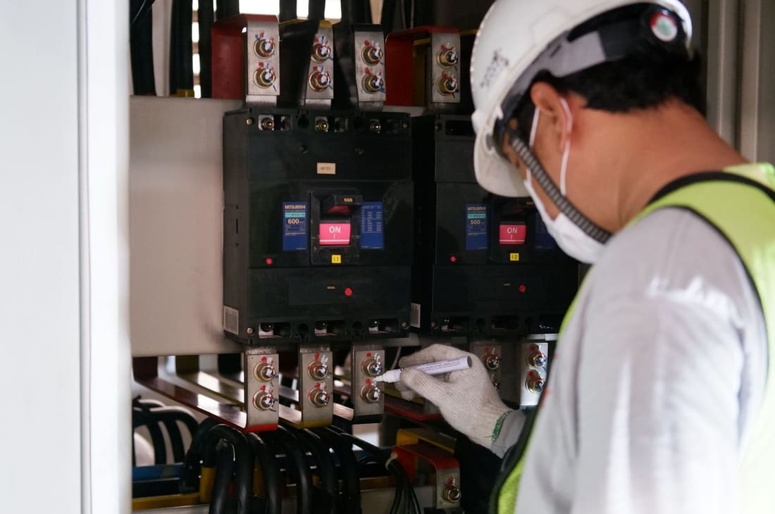 Electrician inspecting moulded-case breakers in a live panel
